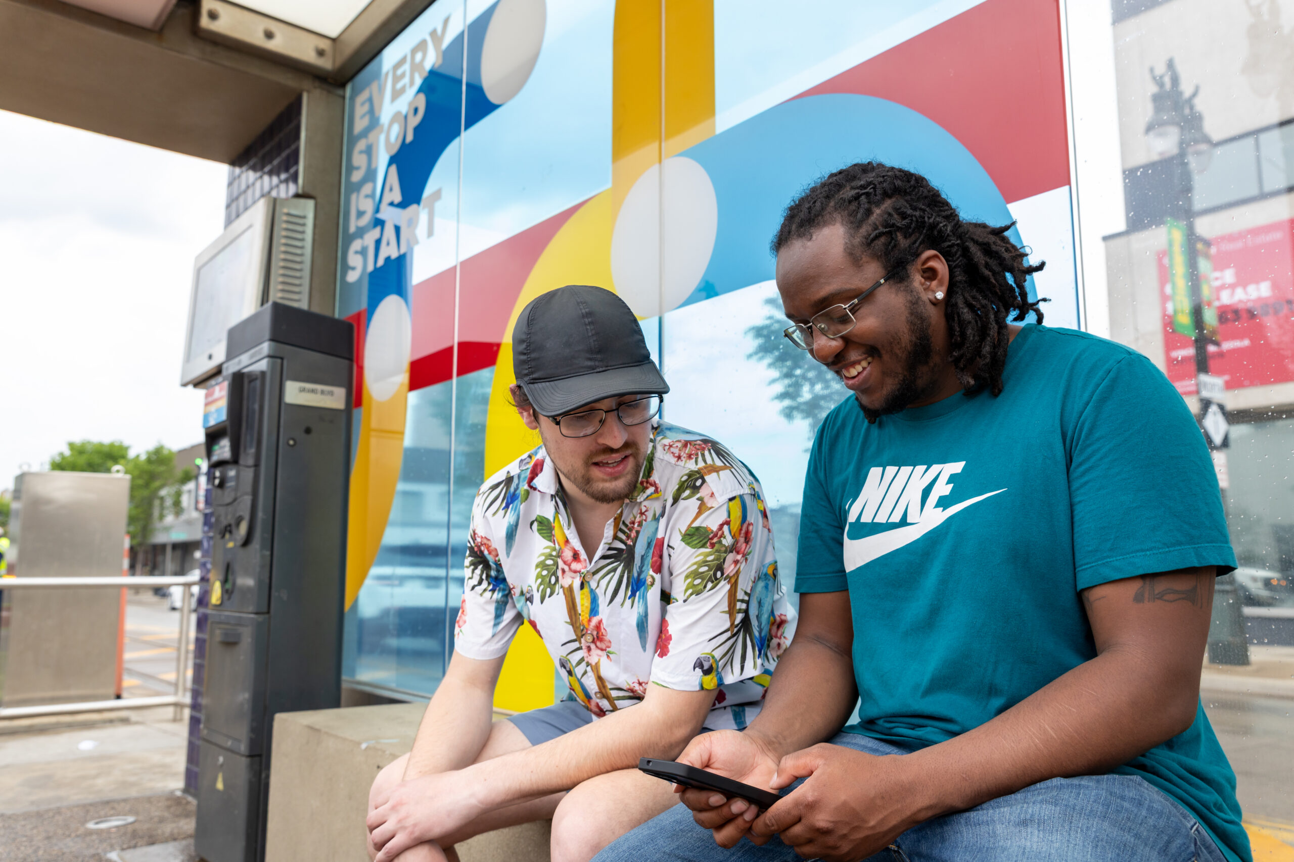 Two friends sit at a QLINE Detroit stop looking at a cellphone